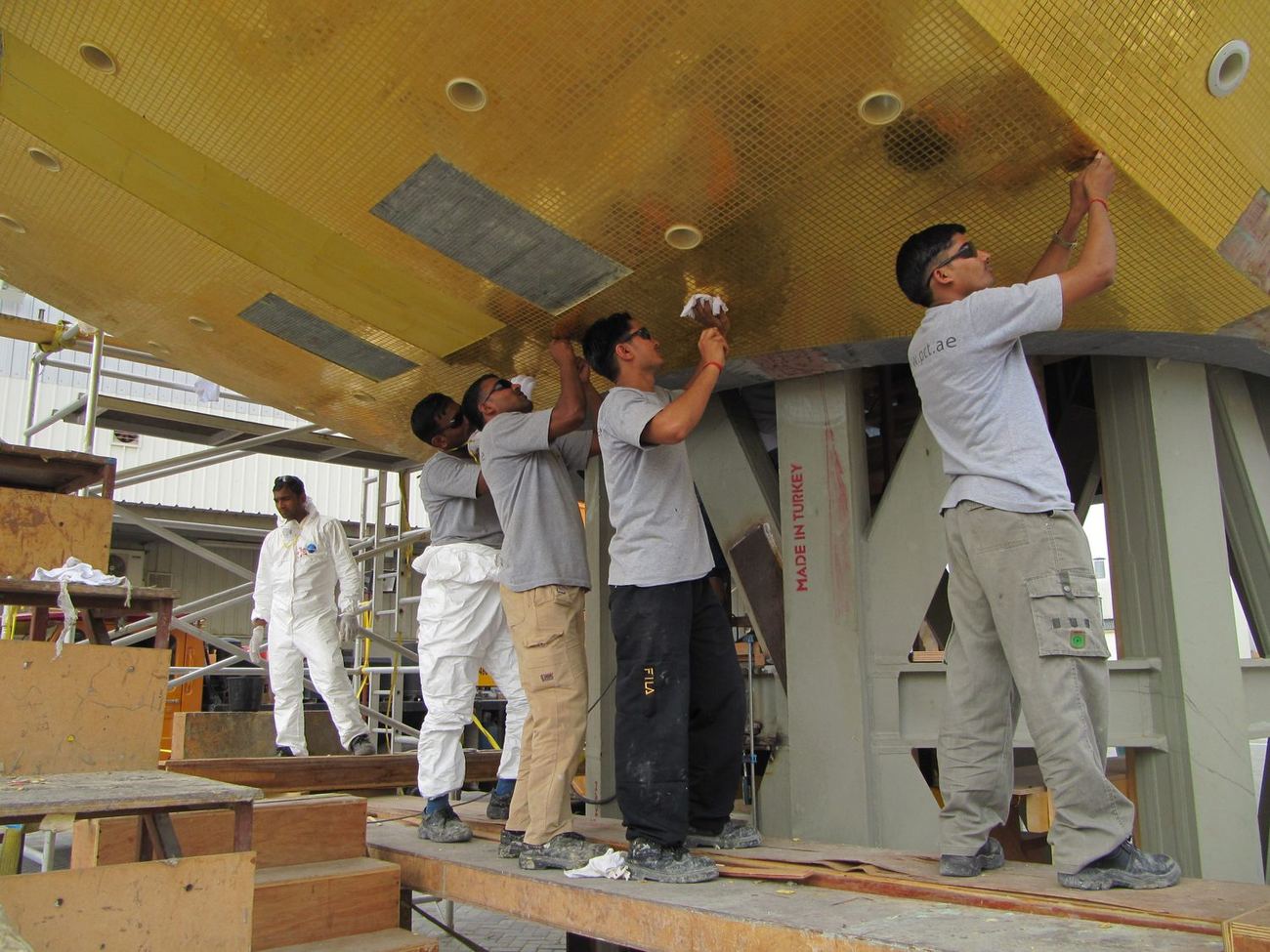 Crew installing gold mosaic panels overhead on a raised platform