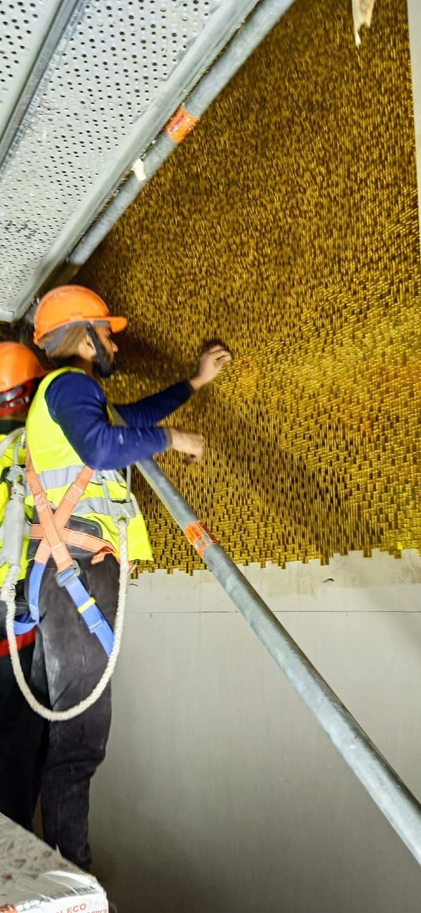 A setter in helmet and harness installing gold mosaic on a wall at height