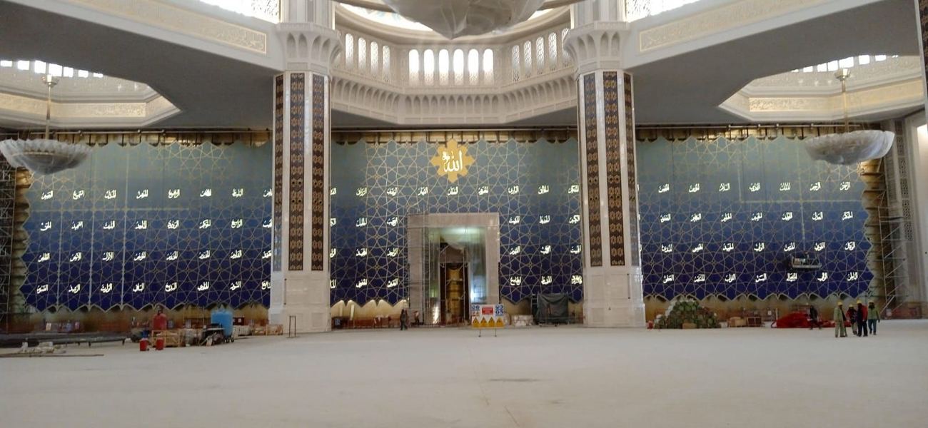 Mosque prayer hall with white columns and a deep blue calligraphic mosaic qibla wall
