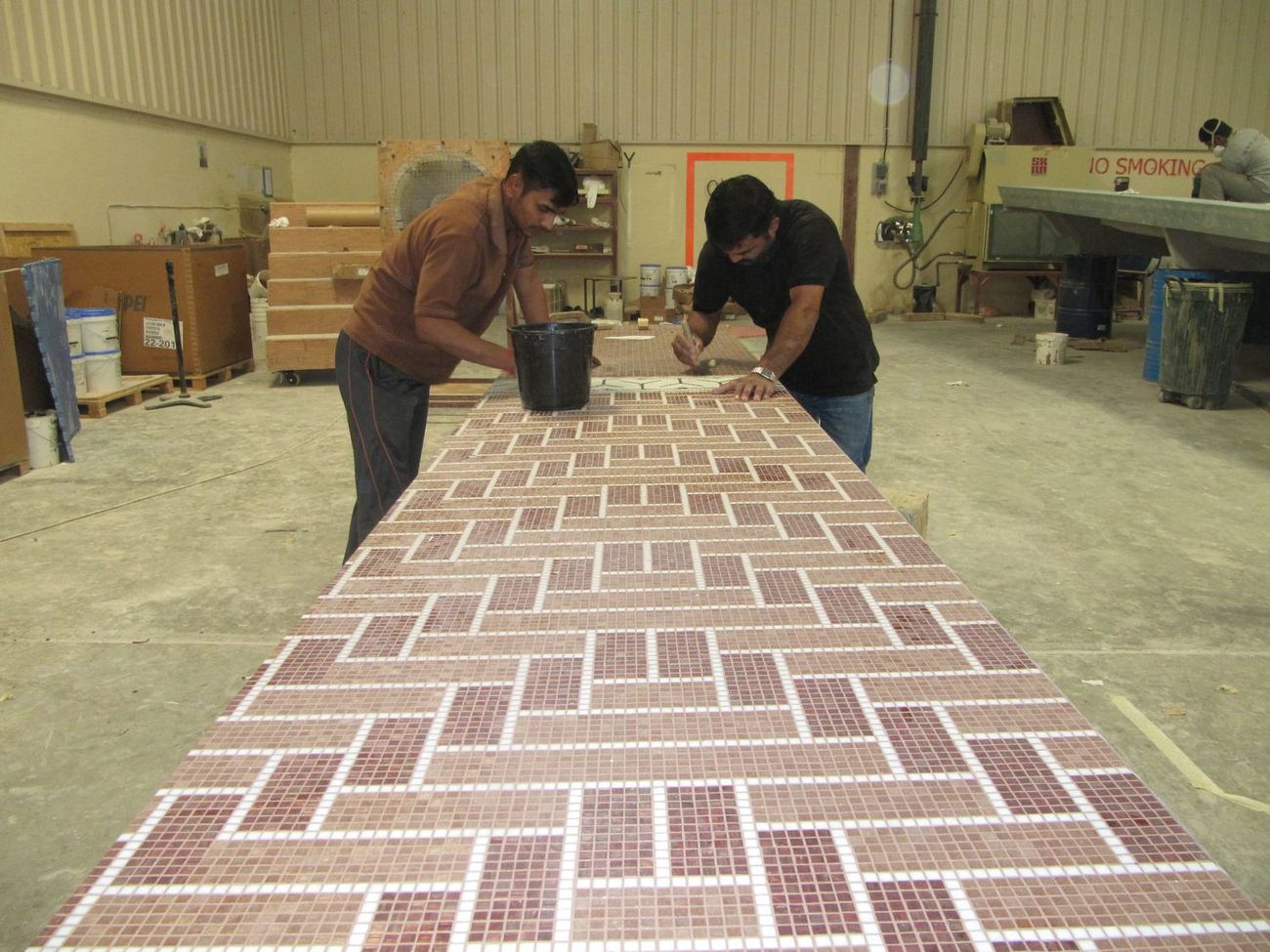 Two setters working along a long mosaic panel on a workshop bench